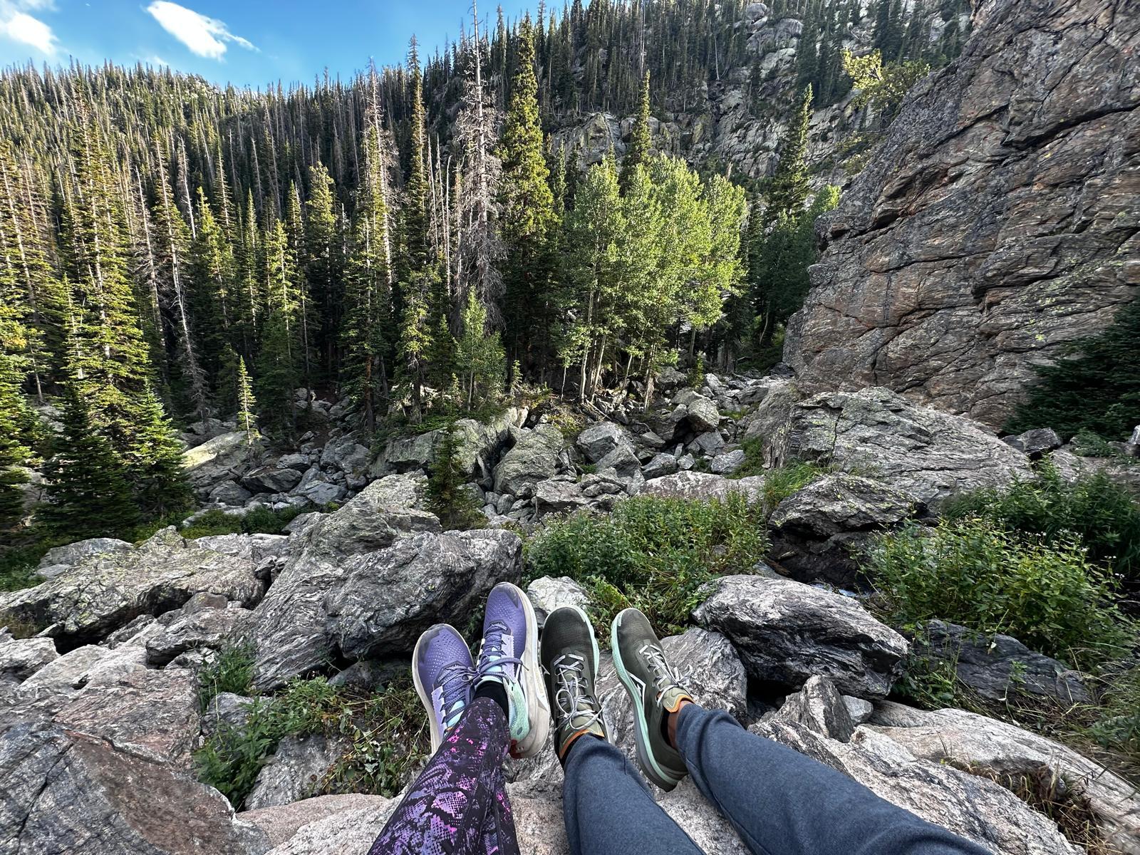 Two hikers resting with their shoes above a rocky forest slope