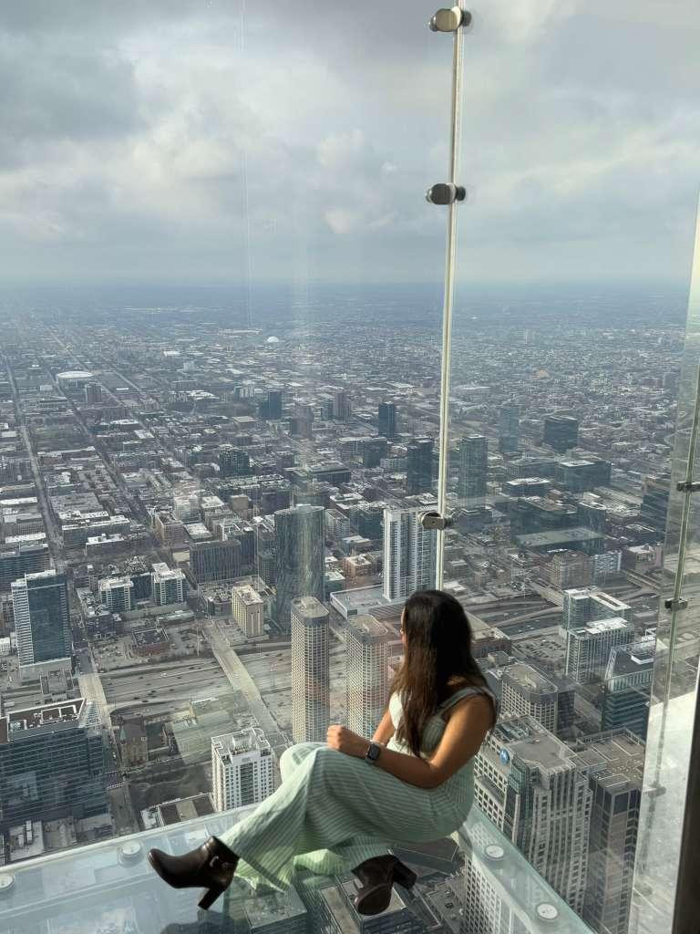 Traveller seated above Chicago inside a glass observation-deck ledge
