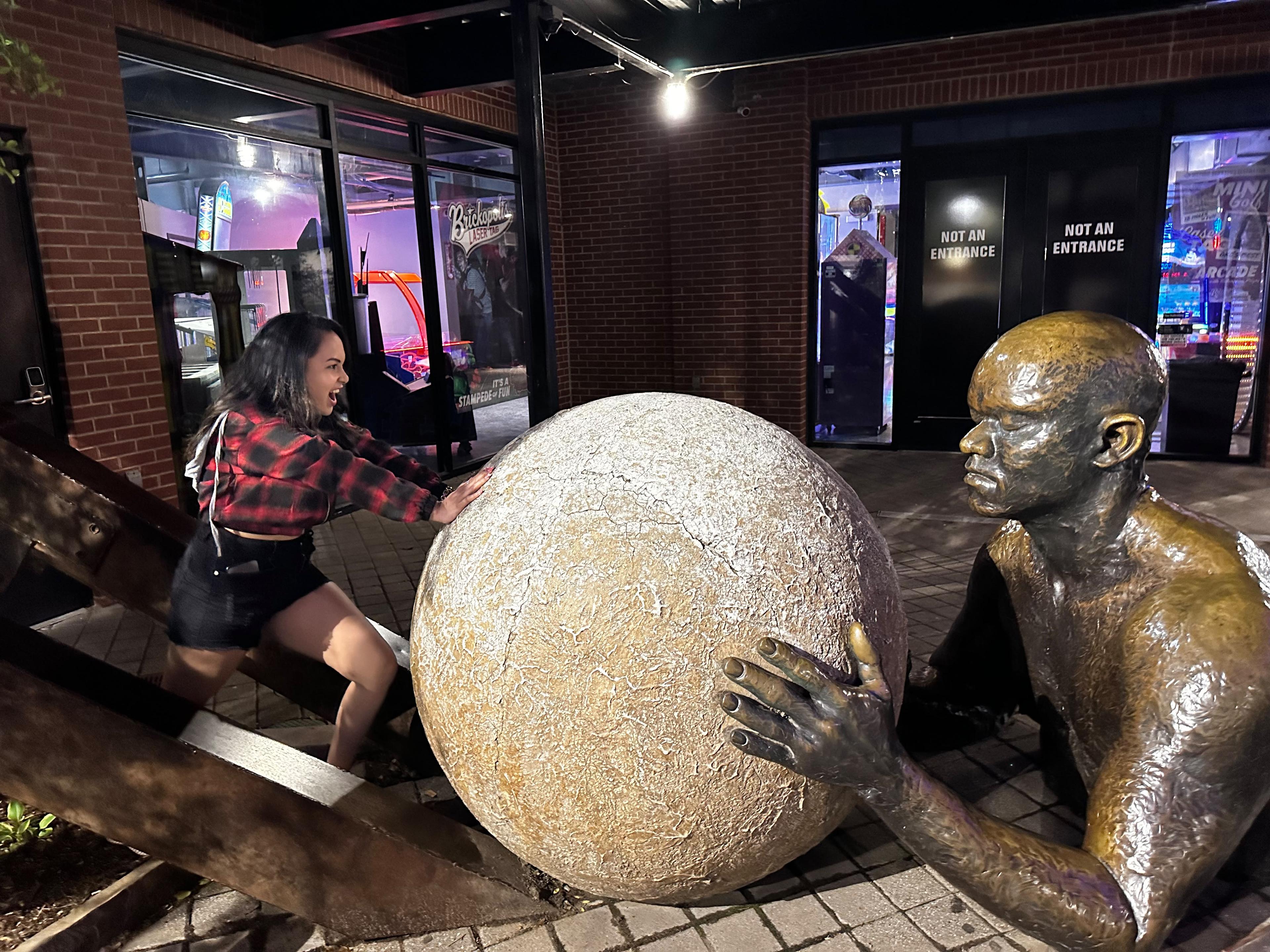 Traveller posing beside a bronze public sculpture holding a large sphere