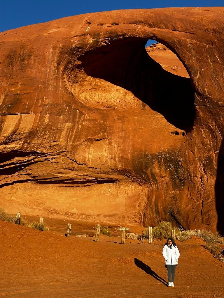 Traveller standing beneath a large Monument Valley sandstone arch