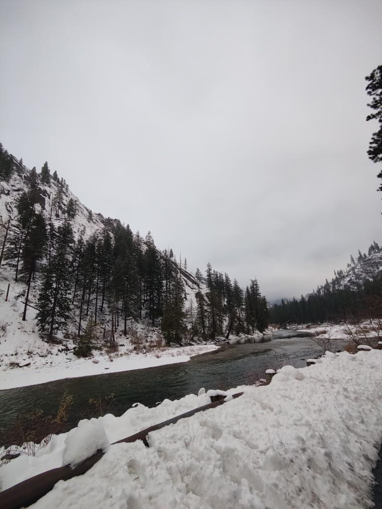 Snow-covered river corridor beneath a cloudy mountain sky